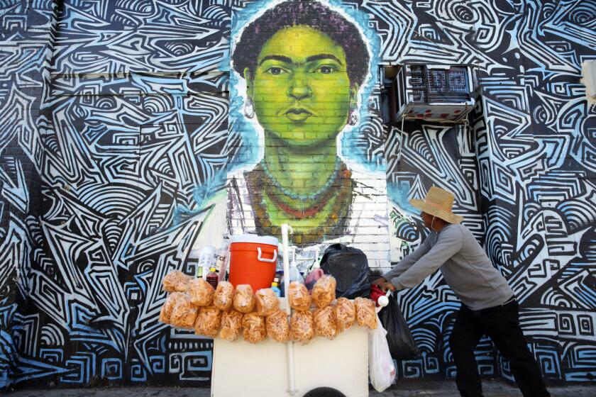 A street vendor pushes a cart past a mural of Frida Kahlo in Los Angeles.