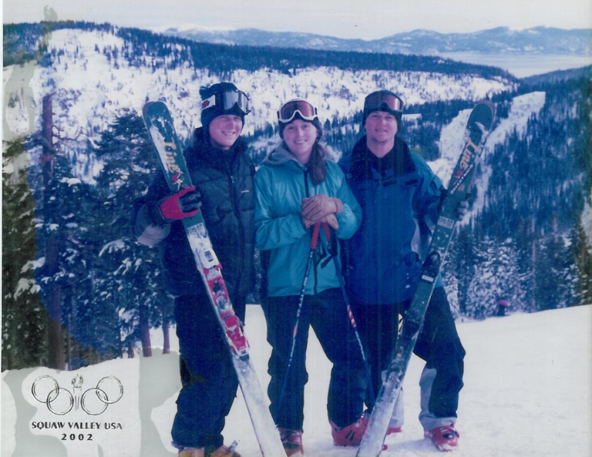 Three young people smile and hold skis.