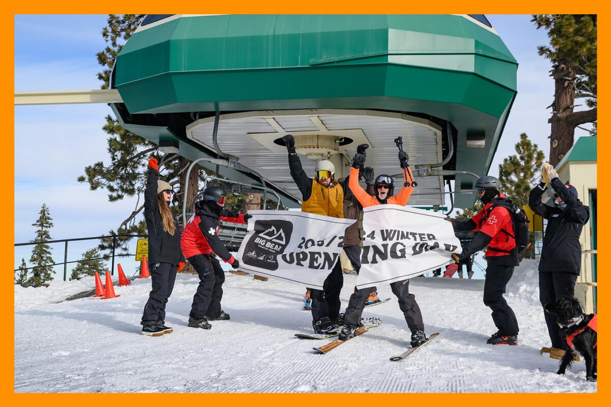 Four people on skis lifting their arms in celebration near a ski lift