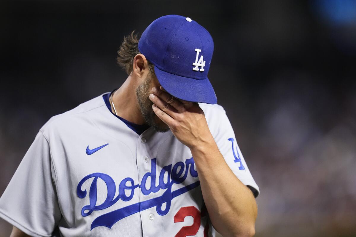 Dodgers starting pitcher Clayton Kershaw walks off the field with his hand over his face.