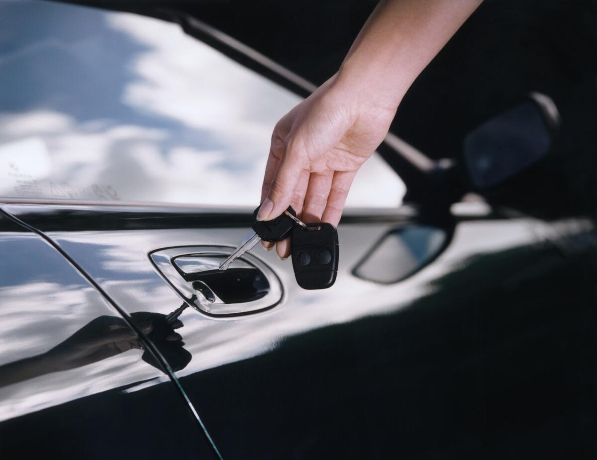 A hand holds car keys next to a car door lock
