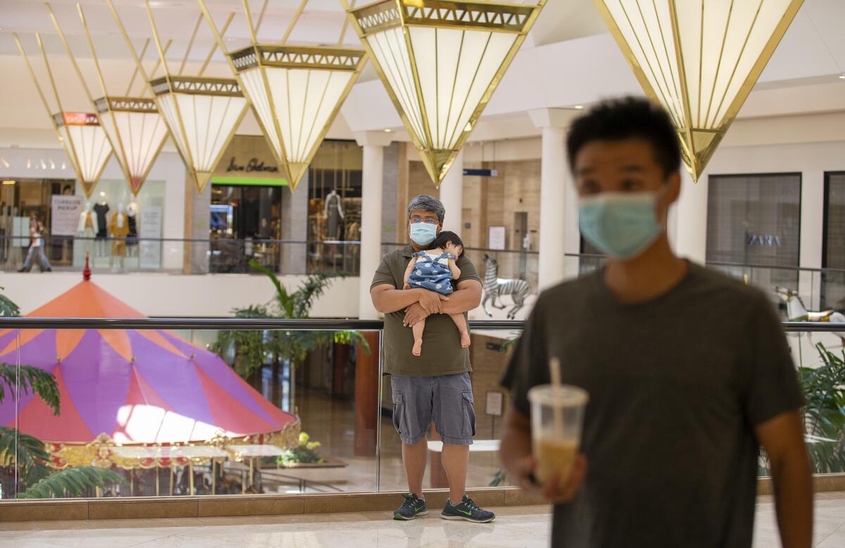 Yasser Zand holds his daughter, Sophia, while waiting for his wife to shop during the reopening of South Coast Plaza.