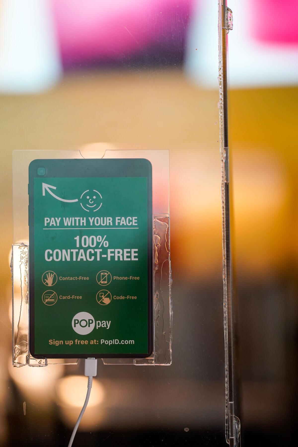 A tablet mounted on a sneeze guard at a Lemonade restaurant advertises the "100% contact-free" Pop Pay system