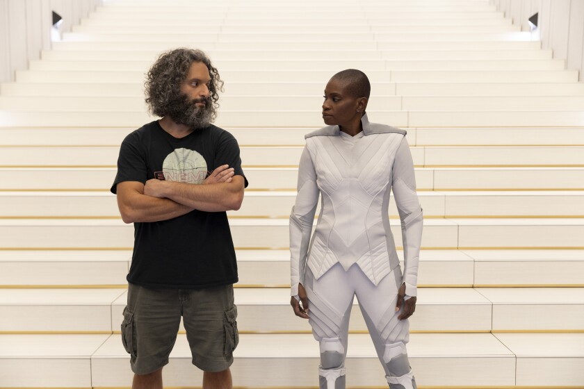 A man in a T-shirt and shorts and a woman in a futuristic white suit 