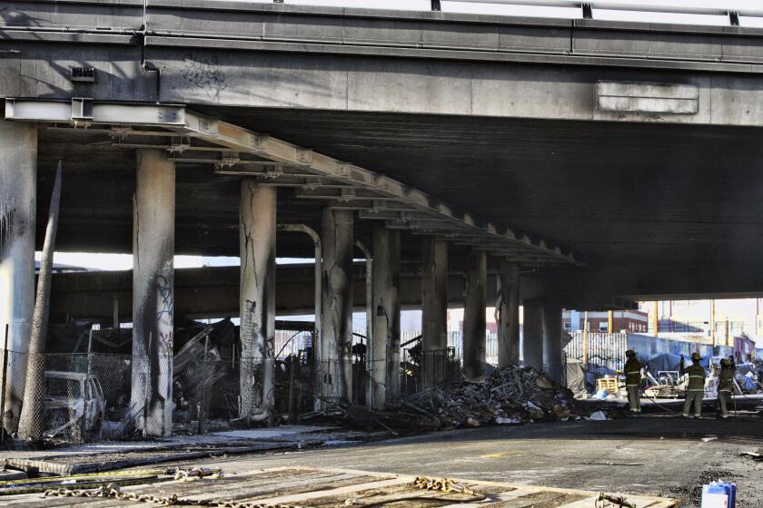 Los bomberos limpian los restos de un incendio bajo la autopista interestatal 10, el cual le causó severos daños a esa vía rápida en una zona industrial, el sábado 11 de noviembre de 2023, cerca del centro de Los Ángeles. (AP Foto/Richard Vogel)