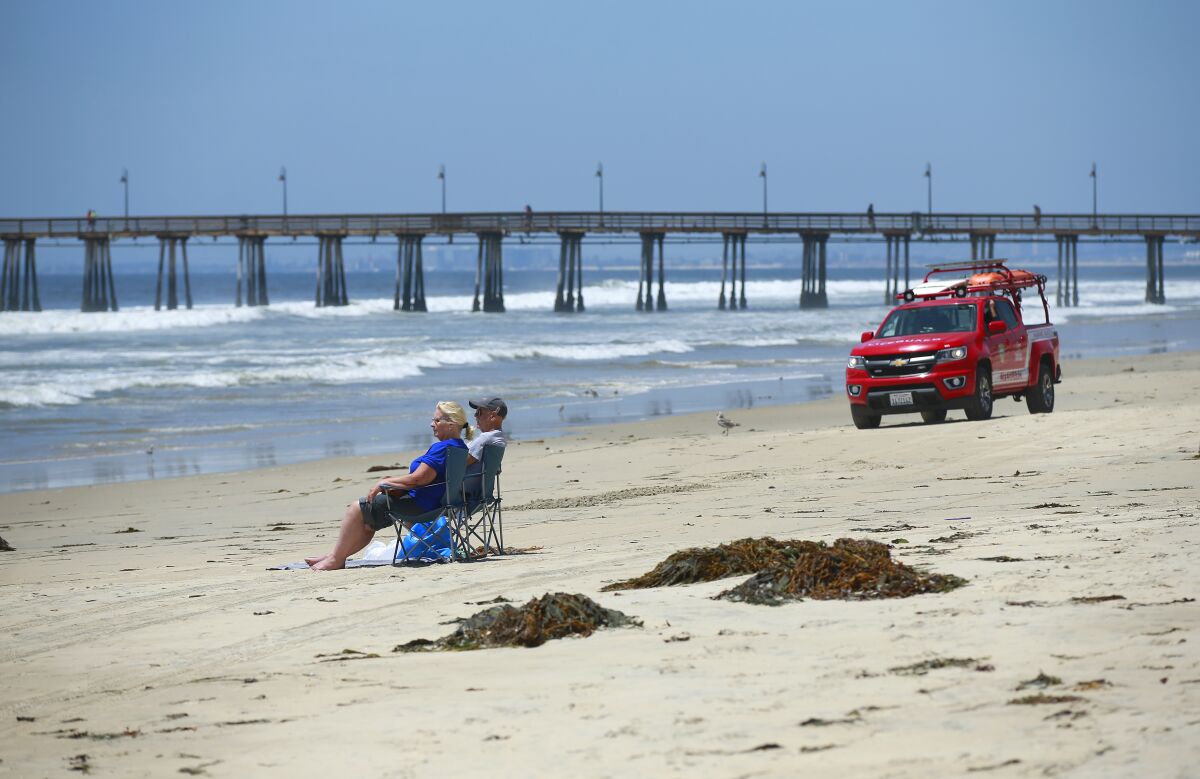 Tourists sit on a nearly empty stretch of beach as lifeguards drive by in Imperial Beach in 2019.
