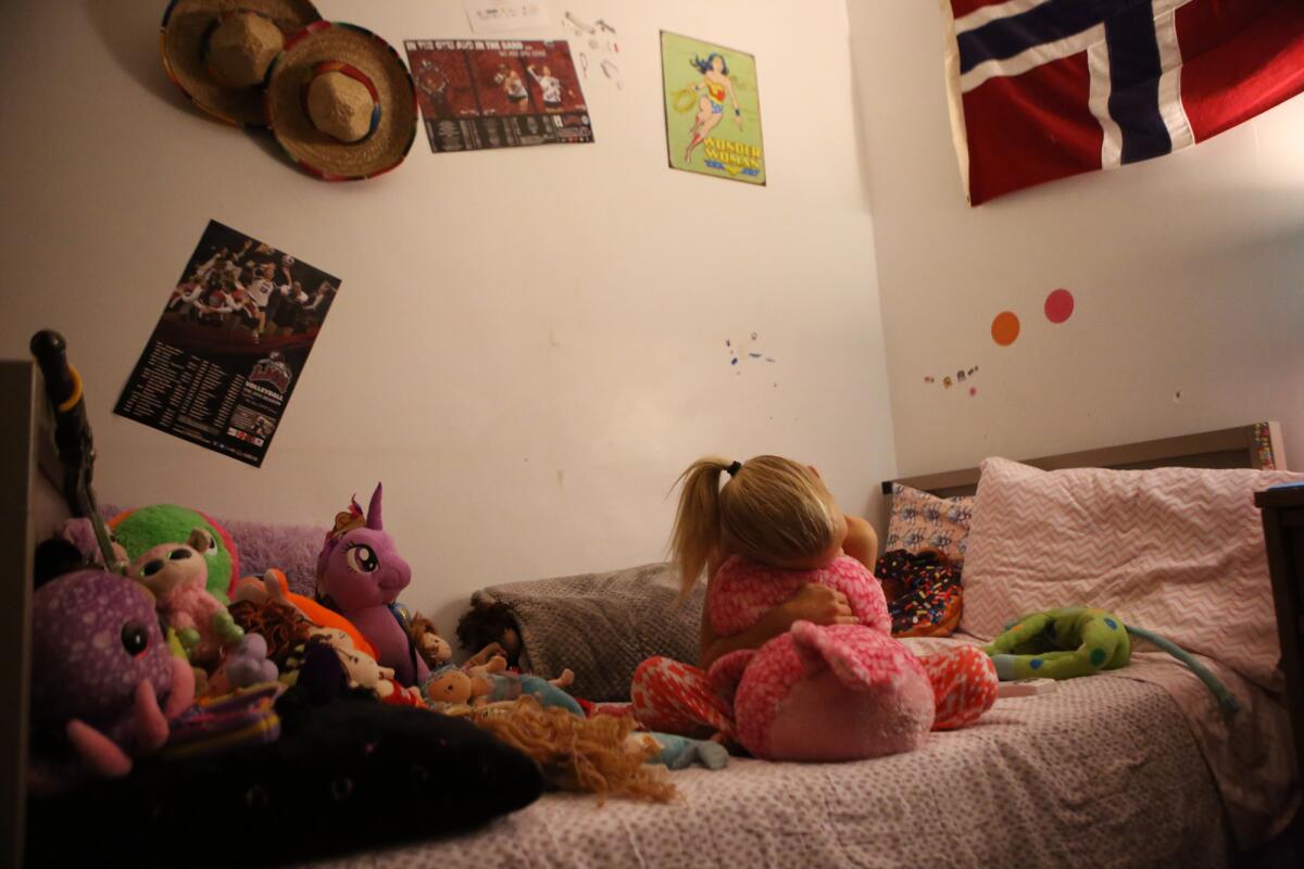 T hugs a stuffed owl on her bed, below a poster of some of her favorite volleyball players. (Genaro Molina / Los Angeles Times)