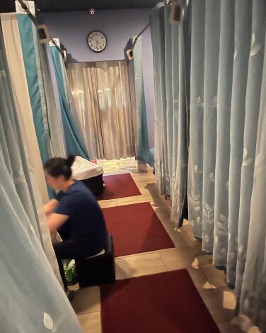 A person sits just outside a curtained room working on the person inside it