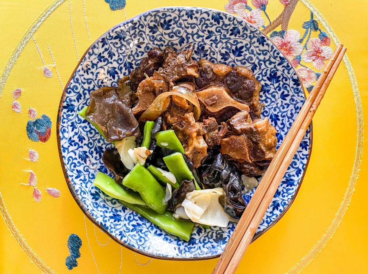 A bowl filled with oxtails in black bean sauce over glass noodles with stir-fried vegetables. 
