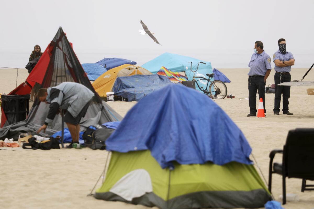 Homeless people break down their encampments on Venice Beach while two county employees watch.