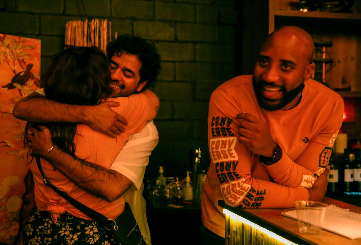 Man hugging woman next to another man smiling behind a bar