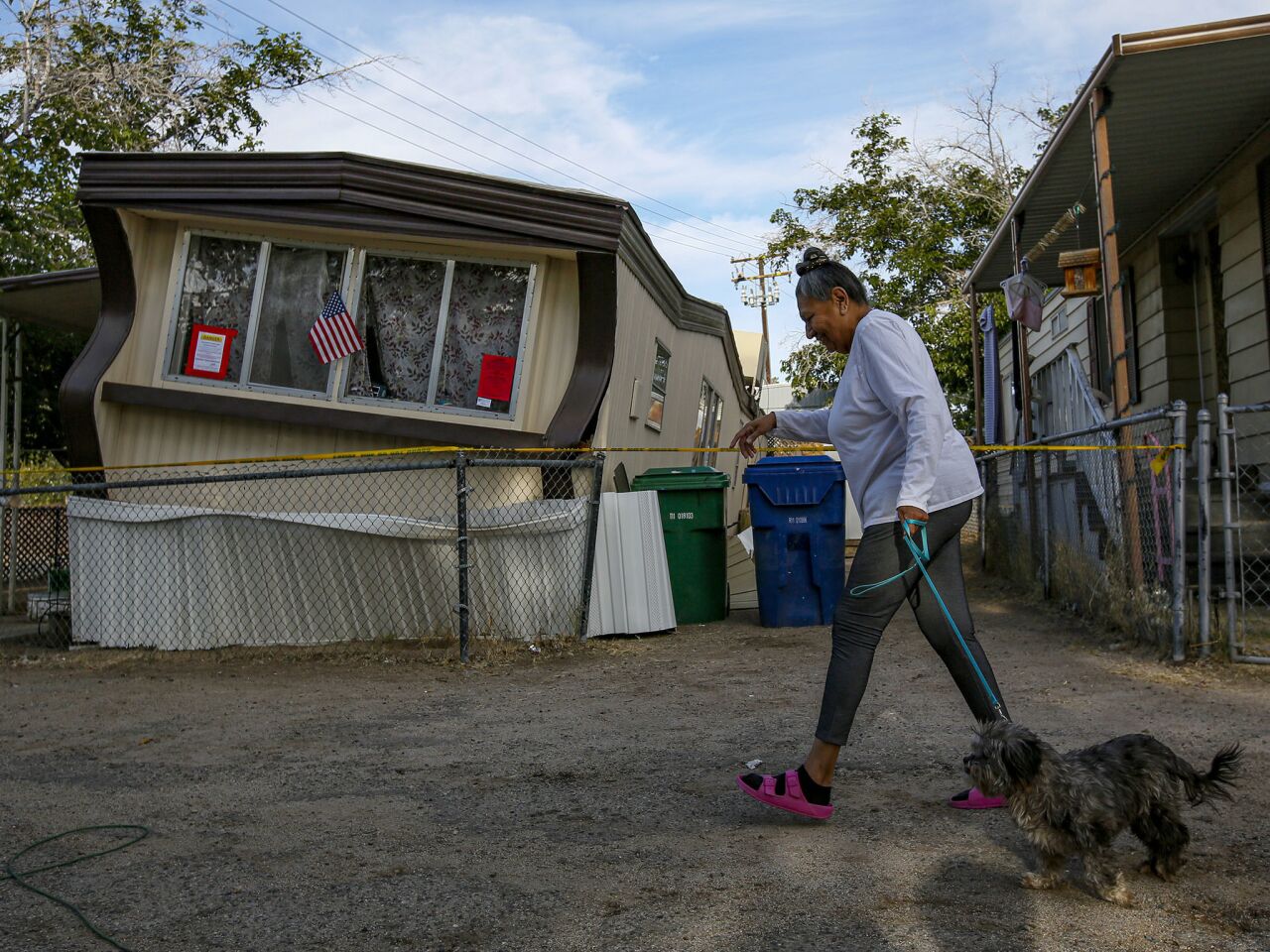Carmen Rivera, 65, walks her dog Ash past a dislodged home in Torusdale Estates mobile home park in Ridgecrest.