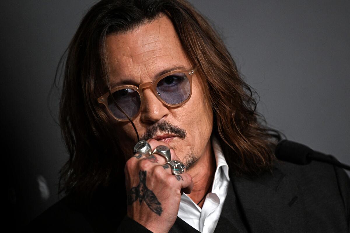 Actor Johnny Depp wearing dark sunglasses and holding a tattooed hand with several rings up to his face
