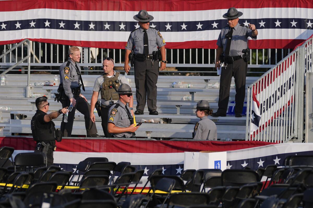 Law enforcement officers examine the campaign rally site in Butler, Pa., where a man shot former President Trump