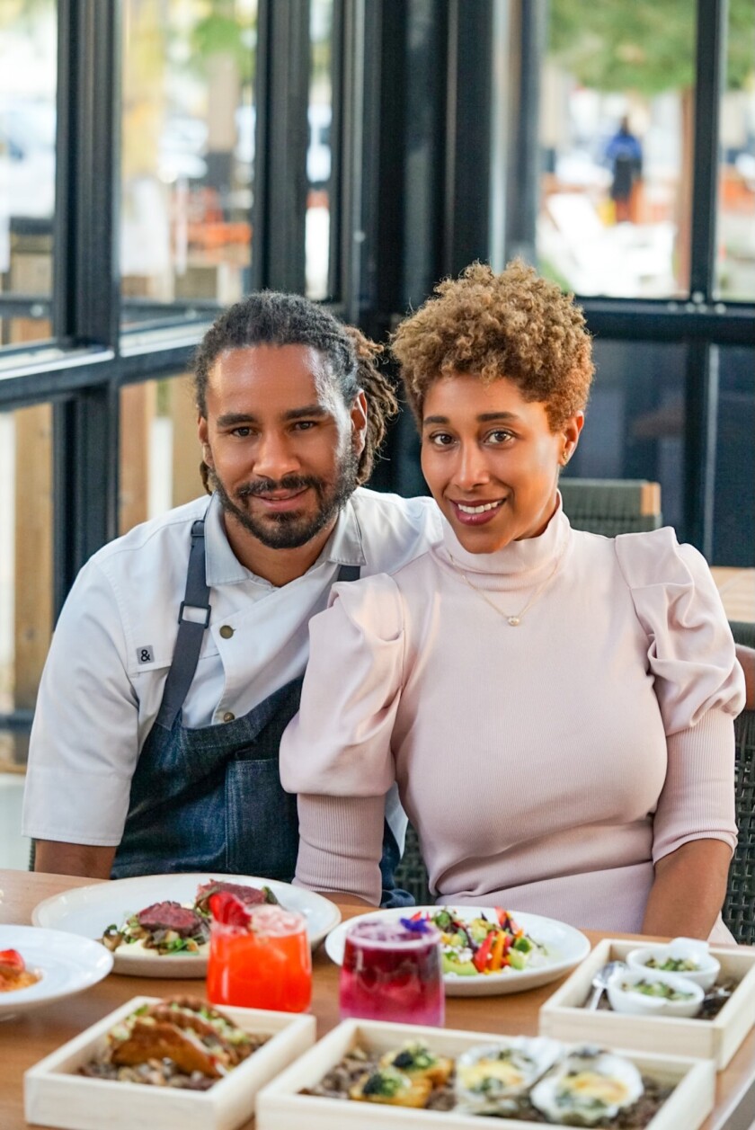 A smiling couple sits at a table of food.