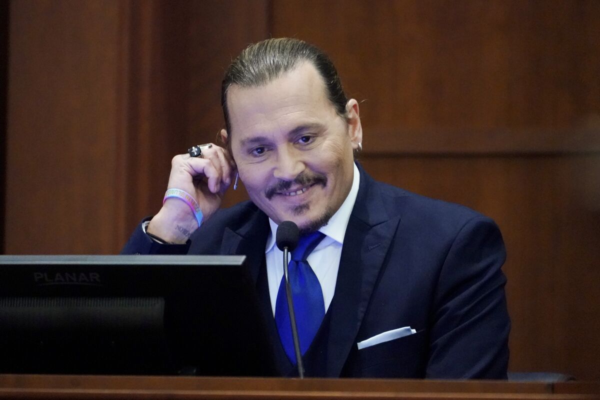 A man smiles and tugs his ear as he testifies in court