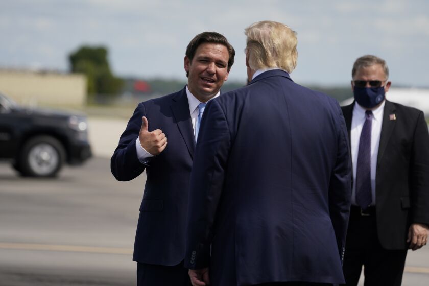 FILE - President Donald Trump speaks with Florida Gov. Ron DeSantis as he arrives at Southwest Florida International Airport, Oct. 16, 2020, in Fort Myers, Fla. (AP Photo/Evan Vucci, File)