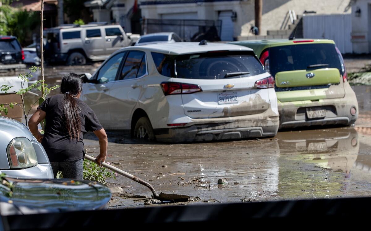 A person holds a shovel in muddy water next to trapped cars.