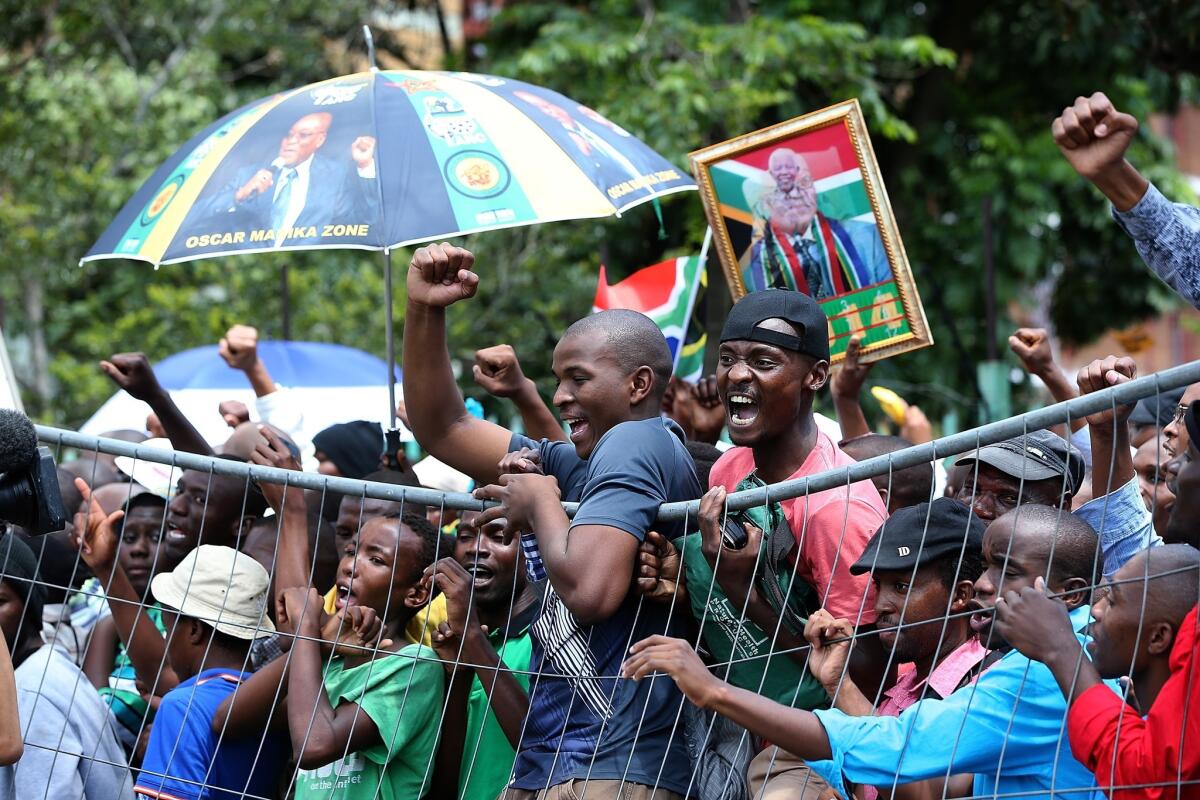 People hang from a fence Friday as they protest outside of the Union Buildings in Pretoria after being told that they would not be allowed access to view the body of former South African President Nelson Mandela as he lied in state.