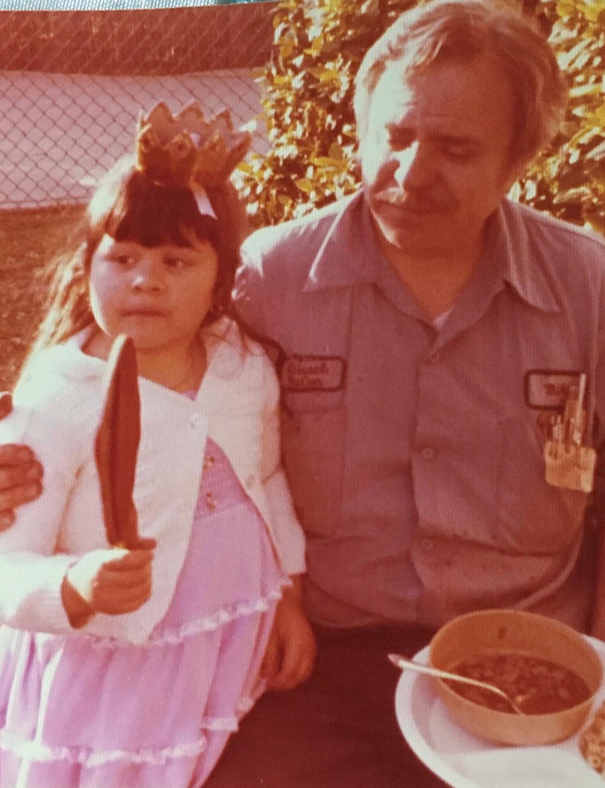An old photo of a grandfather, right, with his arm around a young girl wearing a crown 