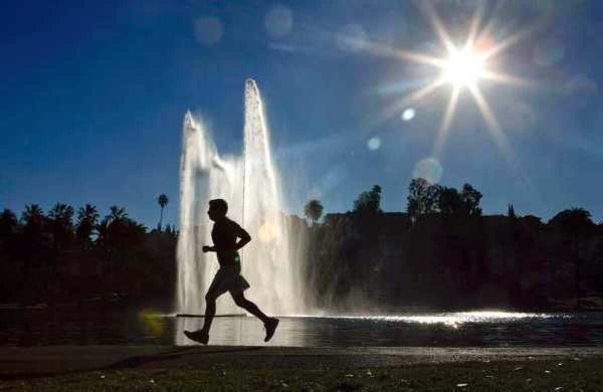 A jogger is silhouetted against a water fountain backdrop at Echo Park Lake in Los Angeles. Summer productivity, already low, will take another hit this holiday week.