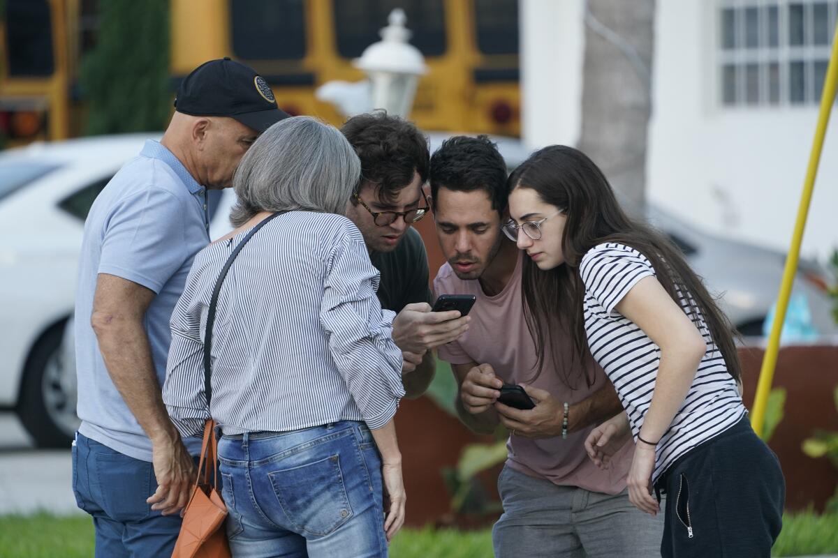 A group of people huddle around a cellphone.