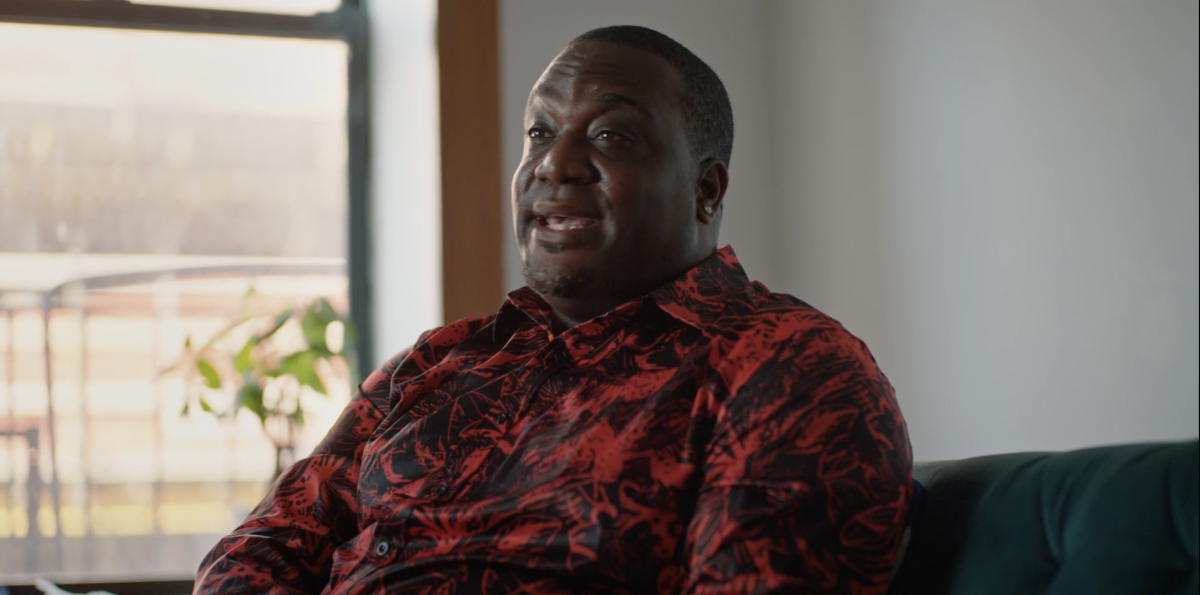 A seated man in a patterned red and black shirt.