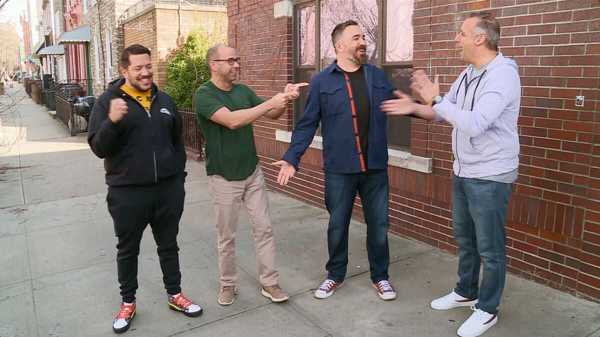 The cast of "Impractical Jokers" standing on a sidewalk outside a brick building.