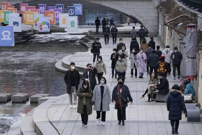 People wearing face masks to help protect against the spread of the coronavirus walk at the Cheonggye Stream in Seoul, South Korea, Monday, Feb. 28, 2022. (AP Photo/Ahn Young-joon)