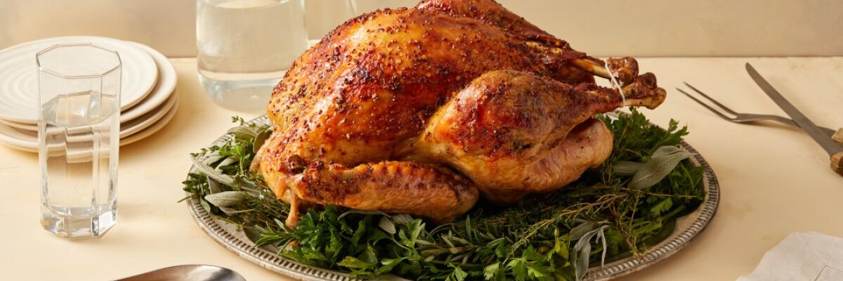 A whole turkey on a silver platter sits atop a dining table alongside a filled gravy boat.