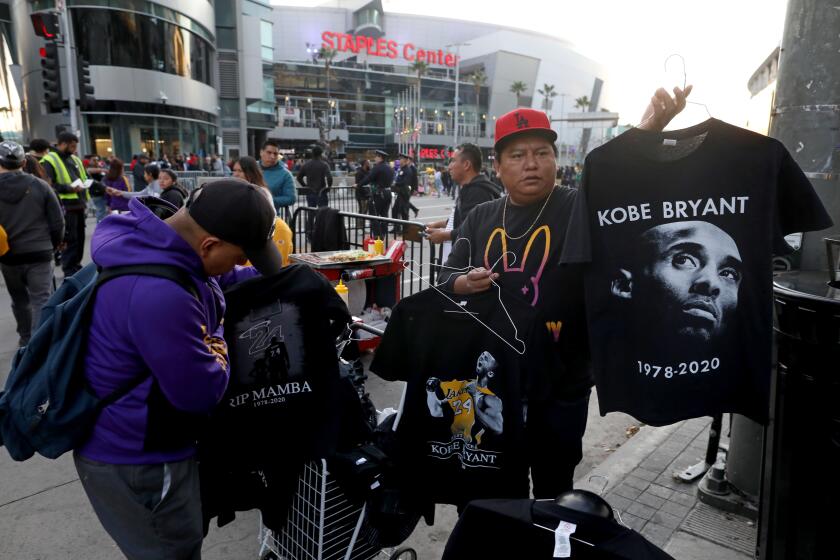 LOS ANGELES, CALIF. -- WEDNESDAY, JANUARY 29, 2020: A street vendor, right, sells Kobe Bryant tee-shirts along Figueroa near the Staples Center in Los Angeles, Calif., on Jan. 29, 2020. Vendors gravitate to Staples Center where — true to L.A. form — sellers of original or knock-off items mingle in and out of the arena’s plaza that has become a shrine of farewell to the basketball legend who died January 26, along with his daughter, pilot, and family friends from Orange County. (Gary Coronado / Los Angeles Times)