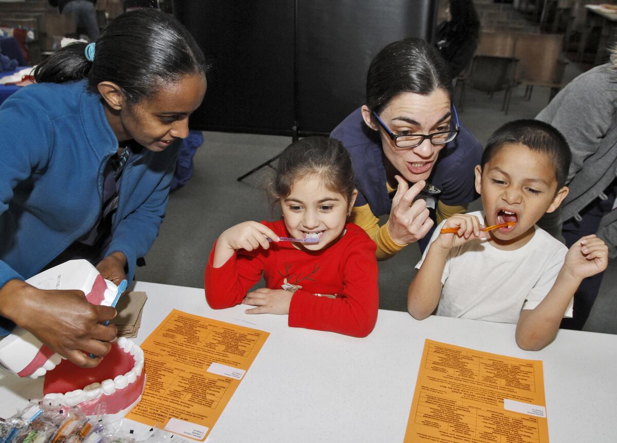 West L.A. College dental hygiene students Tirsit Belew, left, and Leanne Wright, right, show Joaquin Miller Elementary School students Catherine Mkrtchyan, left, and Anthony Sanchez, right, how to properly brush their teeth during the Kids' Community Dental Clinic at the Burbank school on Wednesday, Feb. 25, 2015. The free Give Kids A Smile event provided free dental check up for all the school's students.