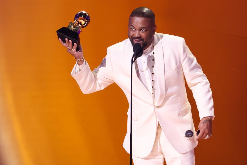 Music producer The-Dream wears a white suit while holding up a Grammy Award onstage