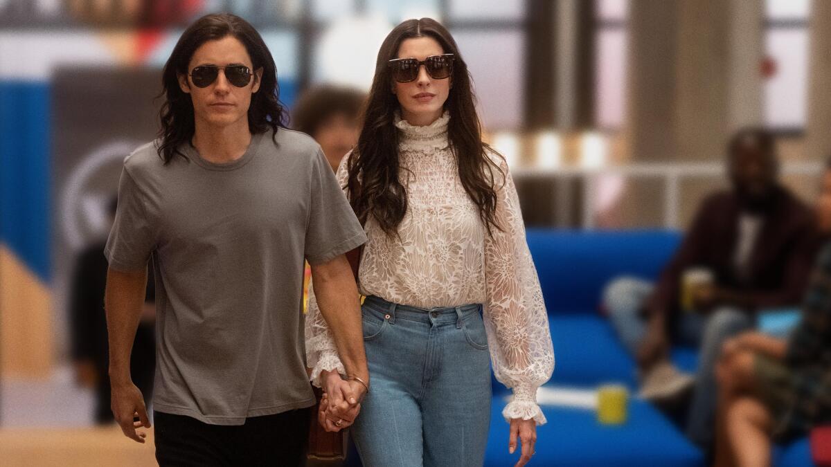 A man and woman walk together holding hands in a scene from "WeCrashed."