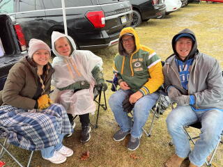 Four people seated in jackets at a tailgate party