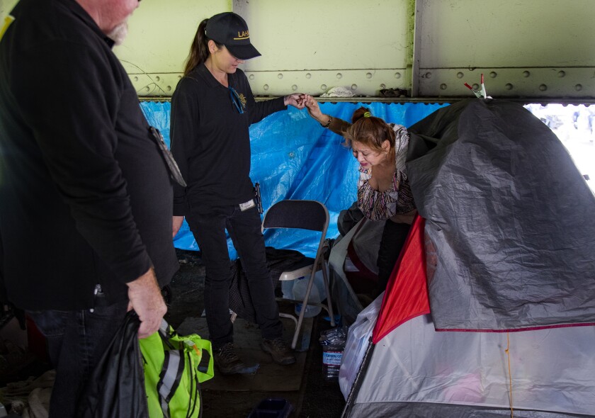 Kelly Doyle, from an L.A. County homeless engagement team, helps Belinda Romero out of her tent under the Valley Boulevard overpass near the San Gabriel River in El Monte. Romero, who said she hadn’t been feeling well, agreed to go a shelter.