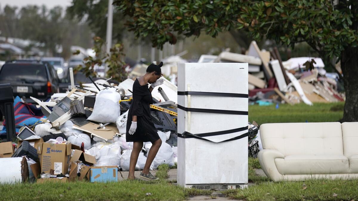 A woman walks among piles of debris, a couch and a refrigerator outside.