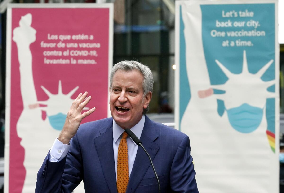 New York Mayor Bill de Blasio delivers remarks flanked by posters of the Statue of Liberty in a mask and bandage on one arm. 