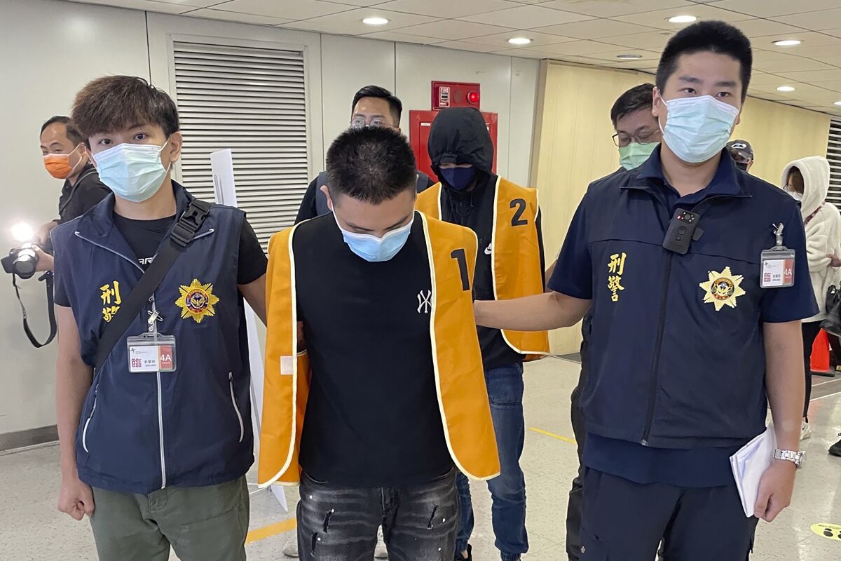 In this photo released by the Taiwan Criminal Investigation Bureau, police officers from the Taiwan Criminal Investigation Bureau escort two suspect who were deported from Bangkok and believed to be involved in scam cases in Cambodia as they arrive back at the Taoyuan International Airport in Taiwan on Thursday, Aug. 18, 2022. Taiwan is seeking to free more than 300 of its citizens lured to Cambodia by organized crime groups promising high wages for tech jobs, but then forcing them into call centers aiming to scam mainland Chinese into making payments for non-existent government fees or investment opportunities. (Taiwan Criminal Investigation Bureau via AP)