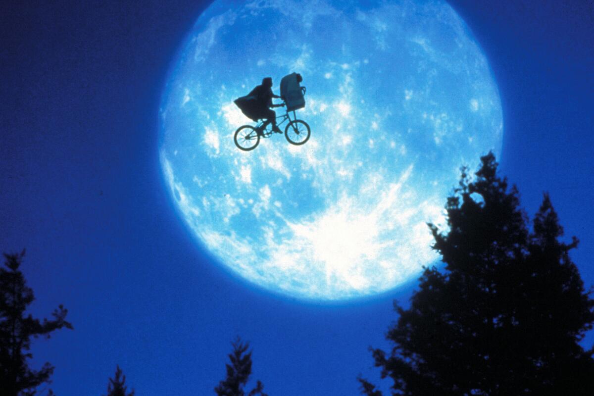 A boy on a bike with a small alien in his basket flying, silhouetted against the moon in the 1982 movie "E.T. the Extra-Terrestrial."