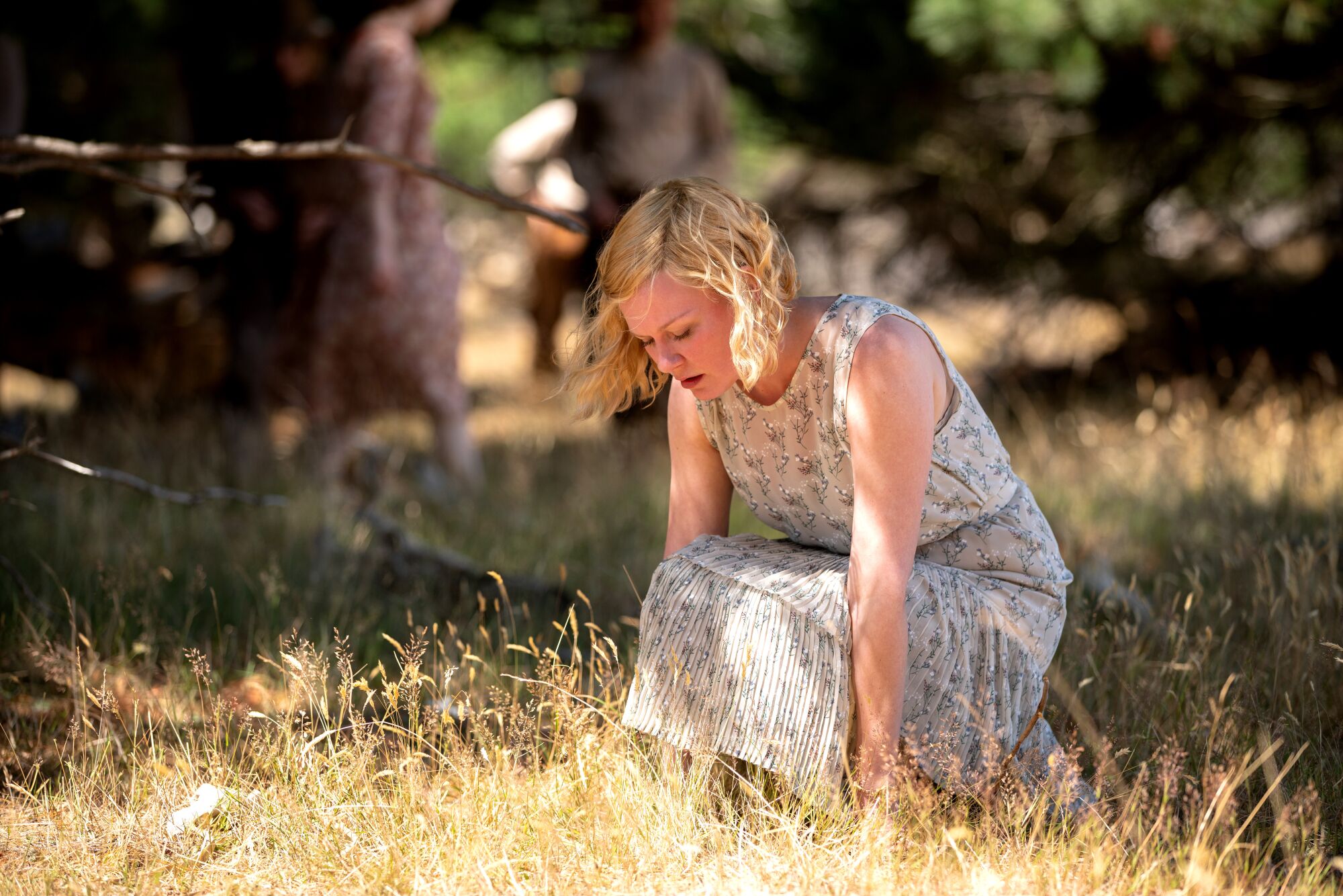 A woman in a floral dress crouches down in grass.