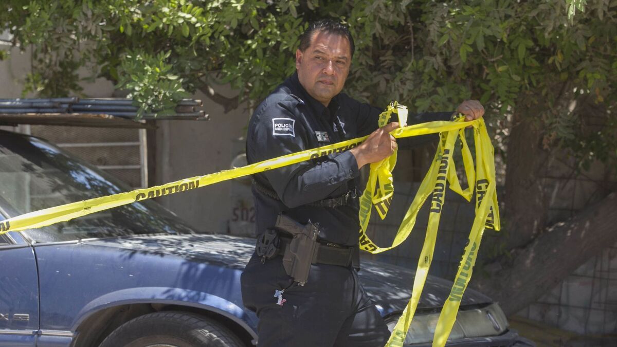 A Tijuana municipal police officer puts up yellow tape at the scene where a woman was gunned down while eating lunch at an outdoor market, File photo.