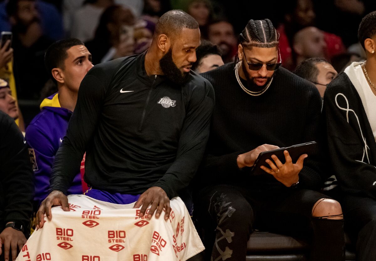 Injured Lakers forward Anthony Davis, right, looks over plays on a tablet with LeBron James.