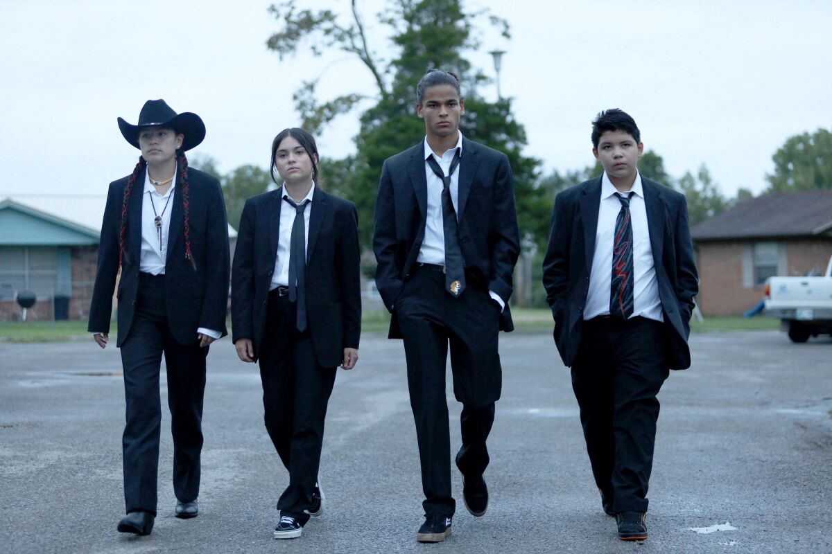 Four teenagers walking in a row dressed in black suits and white shirts