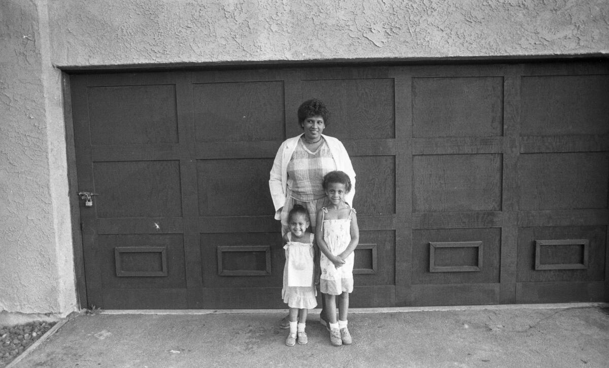 A woman stands in front of a garage door with her two daughters