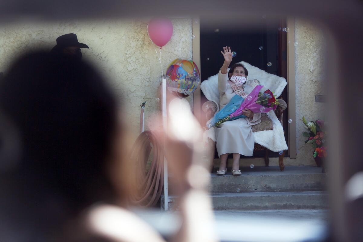 An older woman on a porch with birthday balloons and flowers 