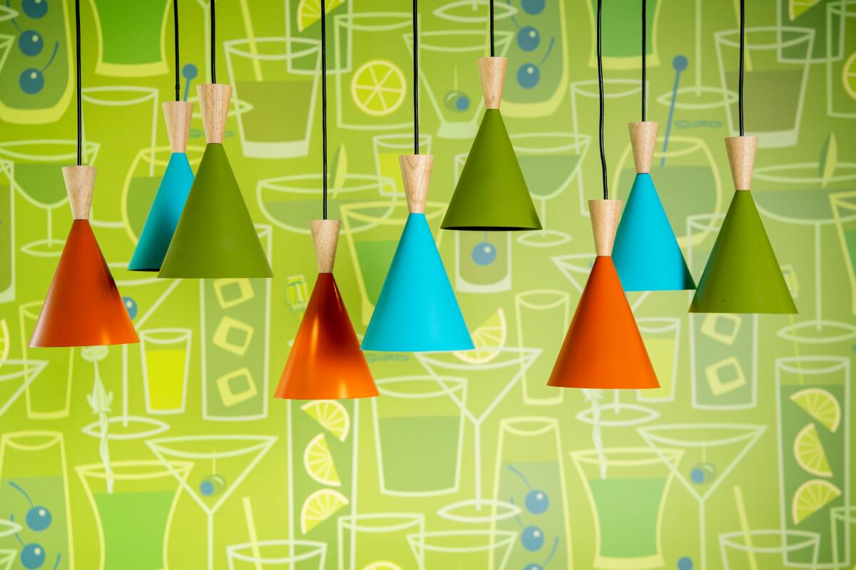 Colorful pendant lights hang in front of a lime green wall decorated with drawings of cocktails