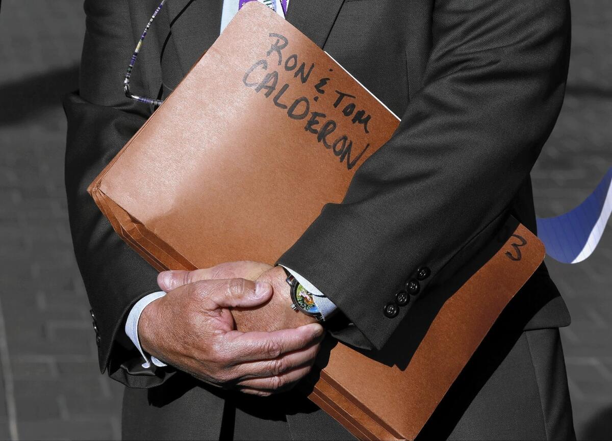 State Department of Justice Public Affairs Officer Thom Mrozek holds a folder tagged with the names of California state Sen. Ronald Calderon and his brother Tom Calderon at a news conference Feb. 24.