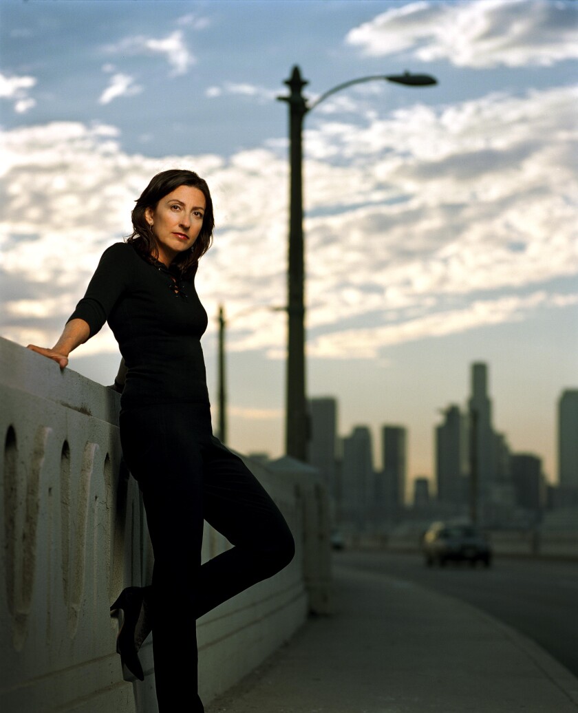 Denise Hamilton stands on a bridge, with downtown Los Angeles visible in the distance.