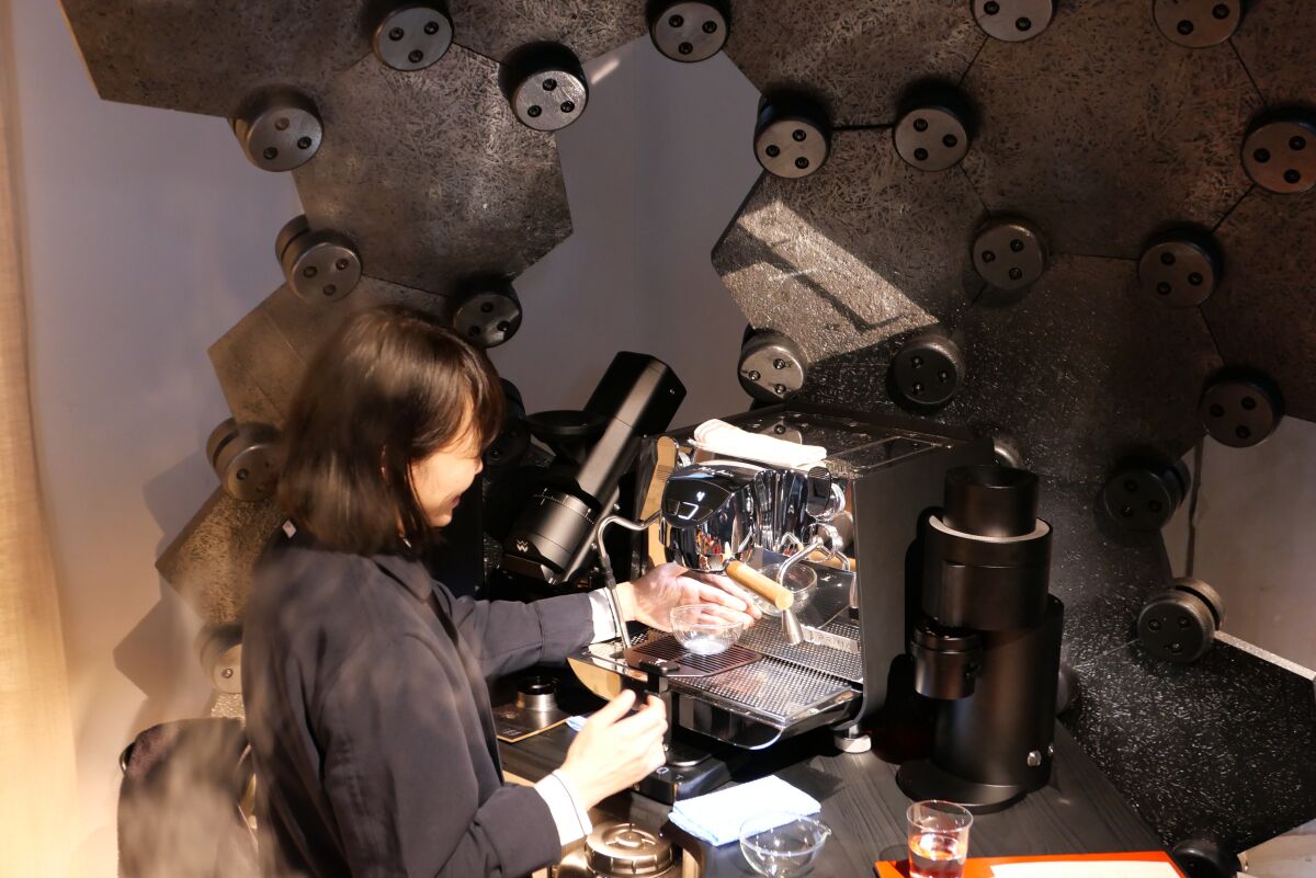 A woman makes a latte at an espresso machine.